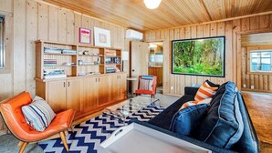 A wooden-paneled room with a sofa, a chair, a bookshelf, and a large window with a view of greenery.