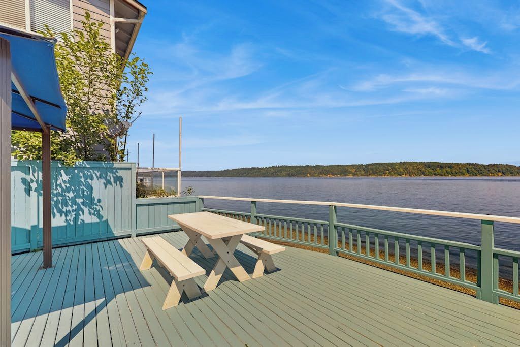 A wooden deck with a picnic table and benches overlooking a lake.