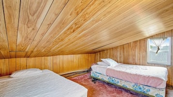A room with wooden walls and ceiling, two beds with floral bedding, and a window with a view.