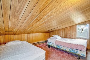 Una habitación con paredes y techo de madera, dos camas con ropa de cama floral y una ventana con vistas.