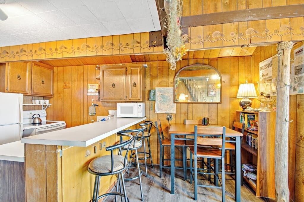 A kitchen with wooden cabinets, a microwave, a sink, and a bar area with stools.