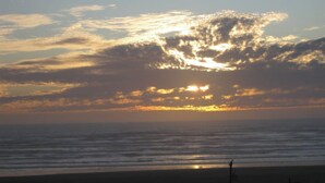 Ein Strand bei Sonnenuntergang, mit Wellen im Meer und einer Person am Ufer.