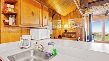 A kitchen with wooden cabinets, a white countertop, a sink, a coffee maker, and a window with a view.