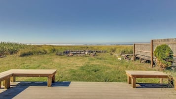 A wooden deck with two benches overlooking a grassy area with a wooden fence and a view of the beach.