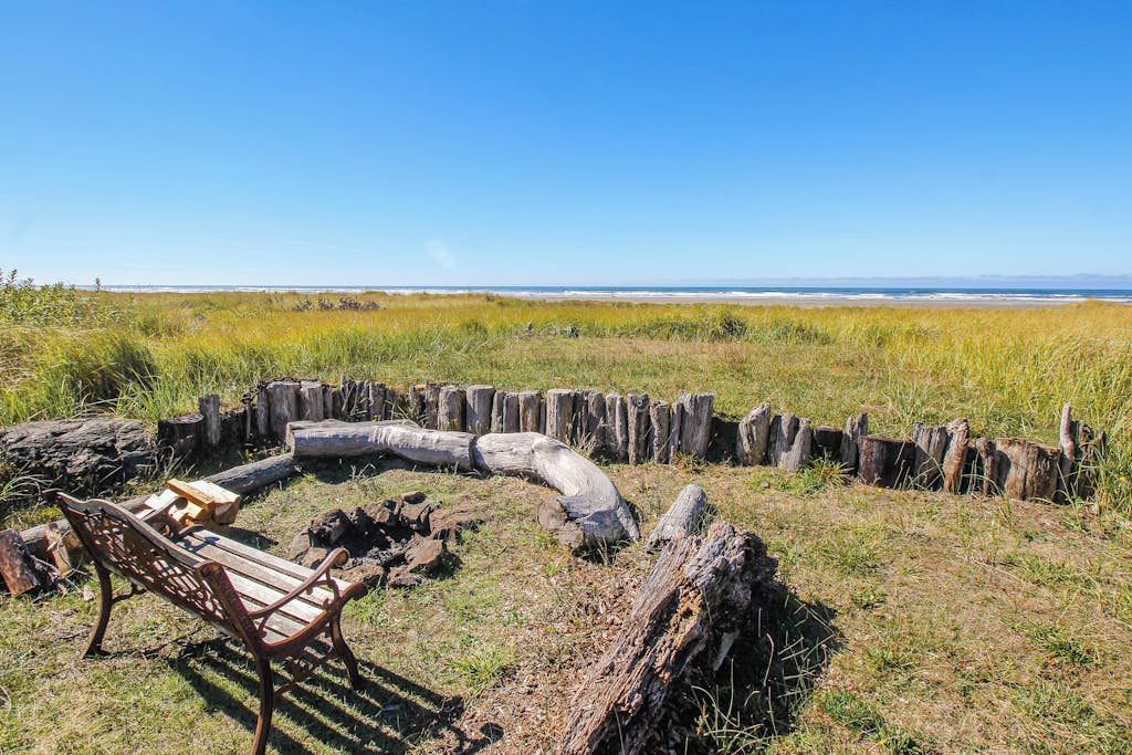 A circular fire pit with a bench, surrounded by a wooden fence, overlooking a beach.