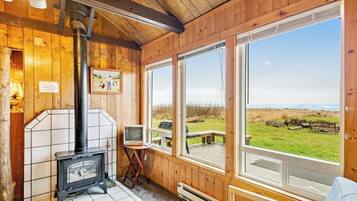 A wooden cabin interior with a fireplace, a television, and large windows overlooking a grassy area.