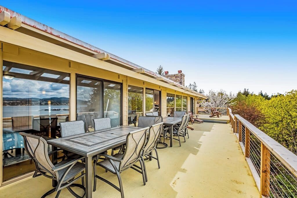 An outdoor dining area with tables and chairs, overlooking a body of water and hills.