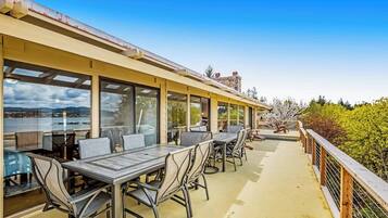 An outdoor dining area with tables and chairs, overlooking a body of water and hills.