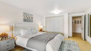 A bedroom with a bed, bedside tables, a nightstand, a wall-mounted artwork, a wardrobe, and a patterned rug.