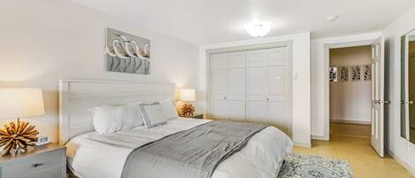 A bedroom with a bed, bedside tables, a nightstand, a wall-mounted artwork, a wardrobe, and a patterned rug.