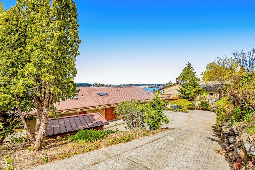 A residential property with a paved driveway, a red-roofed building, and a view of the ocean.
