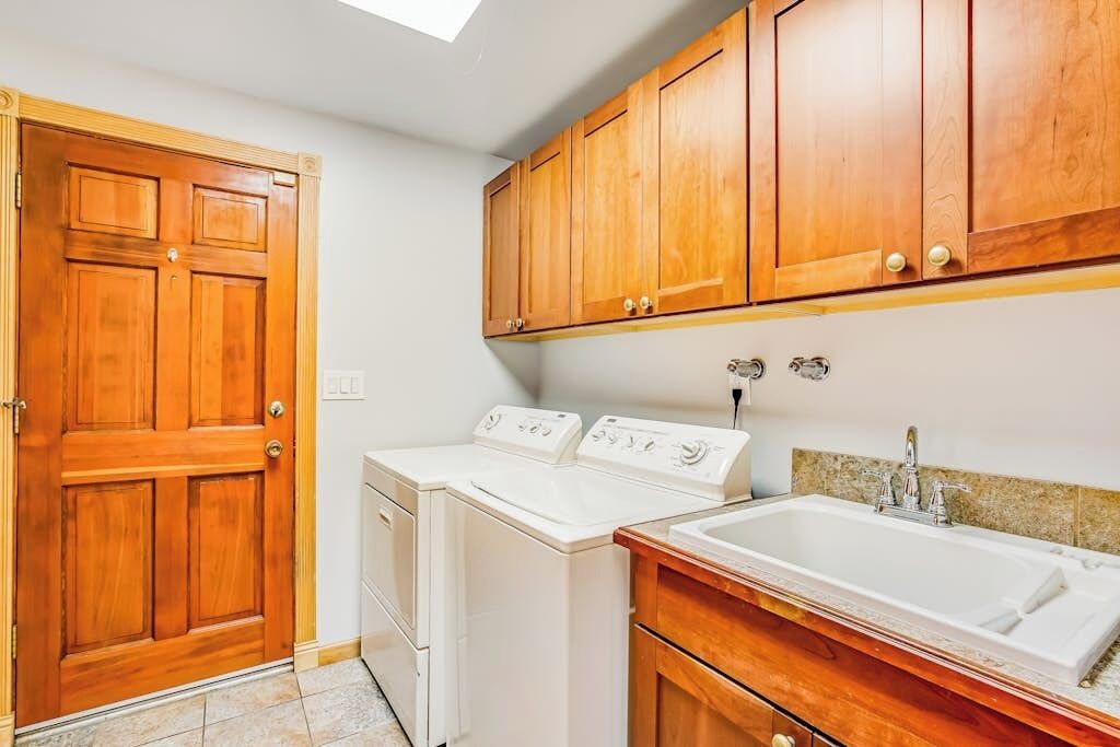 A laundry room with two washing machines, a wooden door, and a sink with a countertop.