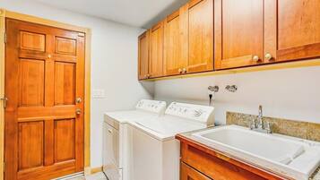 A laundry room with two washing machines, a wooden door, and a sink with a countertop.