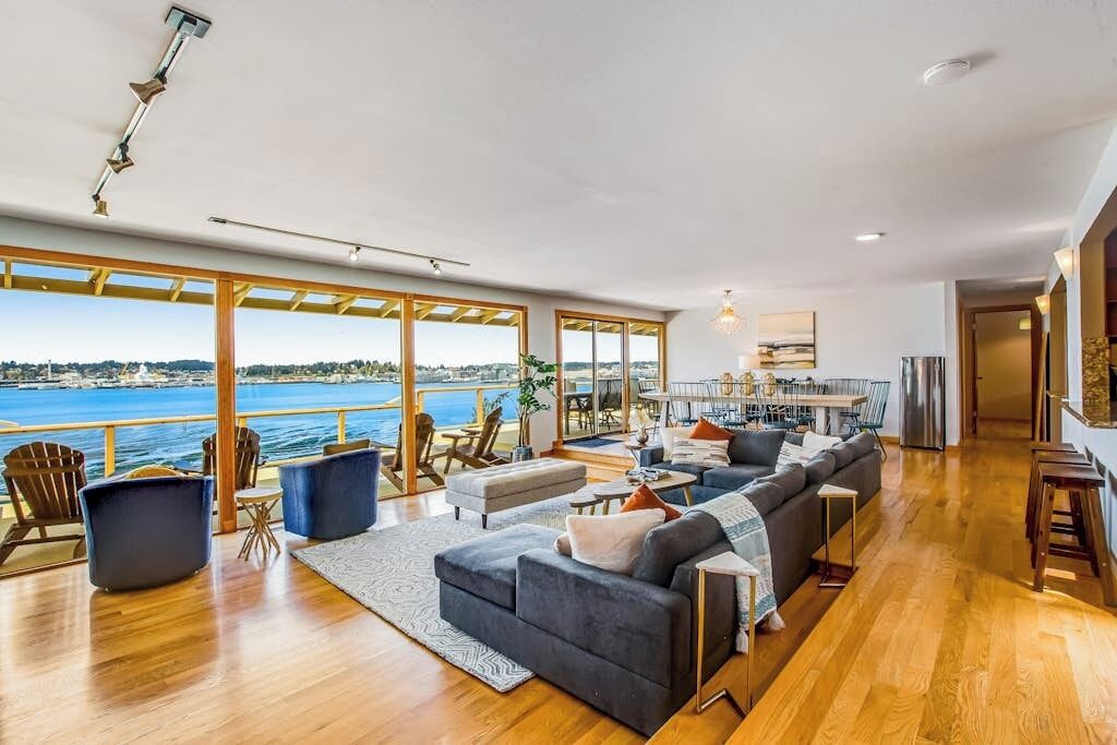 A spacious living area with a large sofa, a dining table, and a view of the sea.