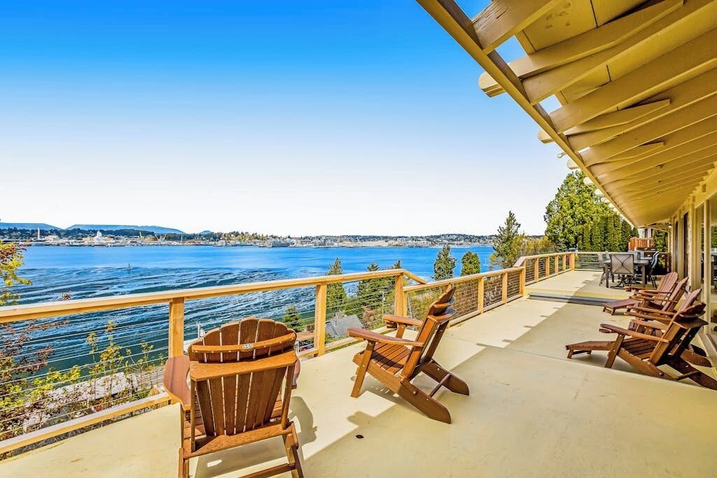 A deck with wooden chairs overlooking a body of water, a clear sky, and distant land.