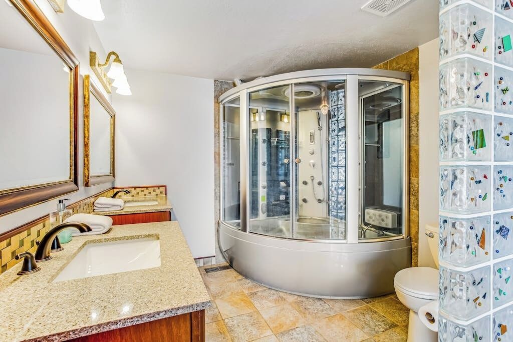 Un baño con cabina de ducha de cristal curvo, lavabo con espejo y un inodoro.