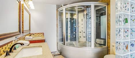 Un baño con cabina de ducha de cristal curvo, lavabo con espejo y un inodoro.