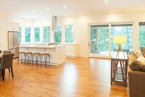 A modern kitchen with a central island, bar stools, and a dining area with a sofa and table. - 4BR tree-lined manor with hot tub, firepit, grill (Cle Elum)