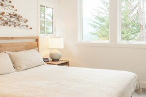 A bedroom with a bed, a nightstand, a lamp, and a window with a view of trees. - 4BR tree-lined manor with hot tub, firepit, grill (Cle Elum)