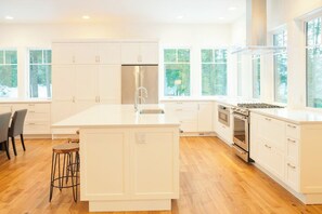 A modern kitchen with white cabinetry, a large island, and a view of the outdoors through large windows. - 4BR tree-lined manor with hot tub, firepit, grill (Cle Elum)