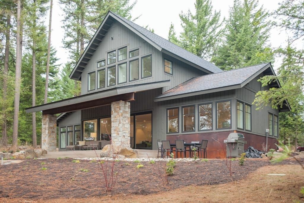 A modern two-story house with a stone foundation, large windows, and a covered patio area.