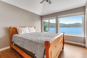 A bedroom with a wooden bed, a view of a lake, and a ceiling fan. - 2BR lakefront home - kayaks, grill, beach access (Olympia)