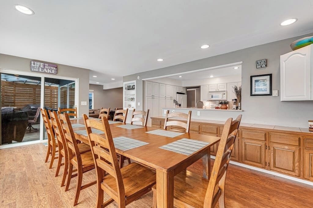 A dining area with a wooden table and chairs, a kitchen in the background, and a sign that reads 'LIFE IS BETTER THE LAKE.'