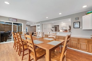 A dining area with a wooden table and chairs, a kitchen in the background, and a sign that reads 'LIFE IS BETTER THE LAKE.' - 2BR lakefront home - kayaks, grill, beach access (Olympia)