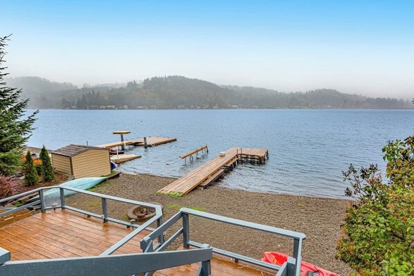 A lakeside deck with wooden walkways leading to docks, a small shed, and a clear view of the water. - 2BR lakefront home - kayaks, grill, beach access (Olympia)