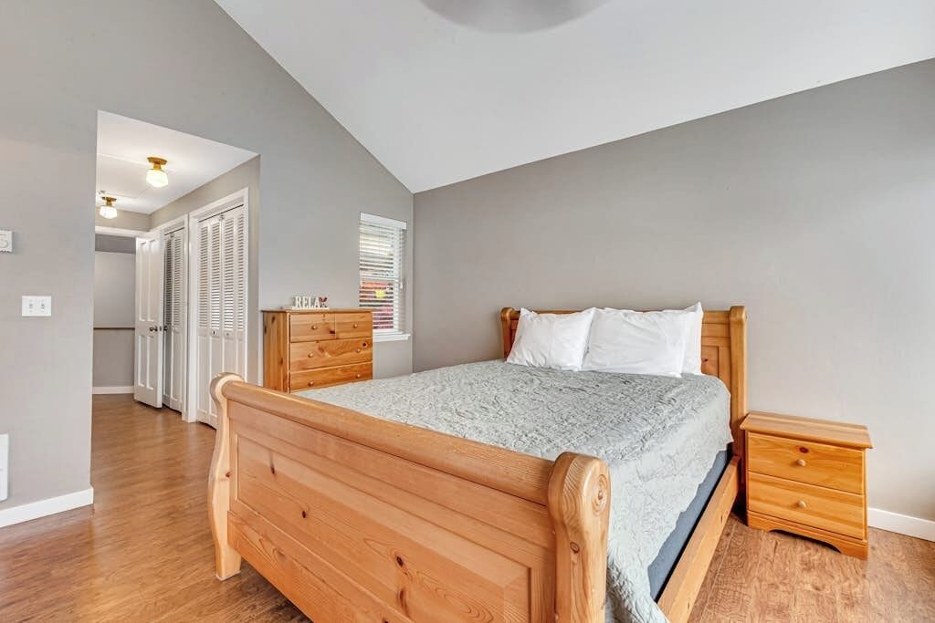 Una camera da letto con un letto di legno, un comodino e una cassettiera. Si apre una porta verso un'altra stanza.