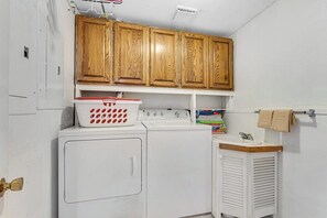 A laundry room with a washing machine, dryer, wooden cabinets, and a small sink. - 2BR lakefront home - kayaks, grill, beach access (Olympia)