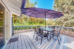 A covered outdoor deck with a table and chairs, surrounded by a wooden railing.