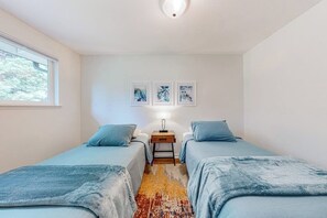 Een kamer met twee bedden, een vloerkleed, een nachtkastje met lamp en drie foto's aan de muur.