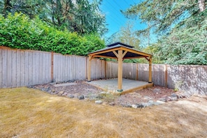 Een houten tuinhuis met betegelde vloer, omringd door een houten hek en een gazon.