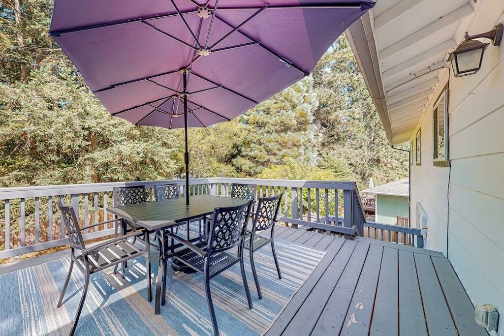 An outdoor deck with a table and chairs, a purple umbrella, and a railing.