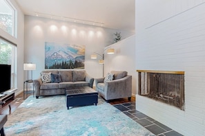 Een moderne woonkamer met een open haard, een zithoek en een groot schilderij aan de muur.