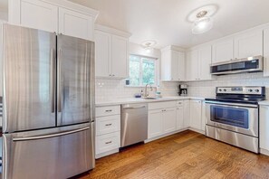 A modern kitchen with stainless steel appliances, white cabinetry, and a wooden floor.
