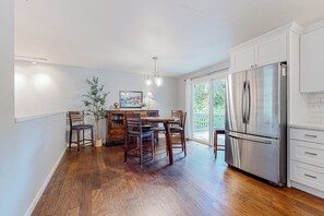 A kitchen with a dining table, chairs, a refrigerator, and a potted plant.