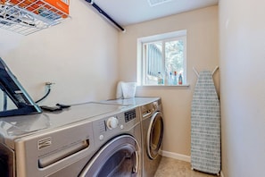 A compact laundry area with a front-loading washer and dryer, a drying rack, and a window providing natural light.