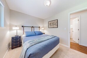A bedroom with a bed, bedside lamps, a map artwork, a suitcase, and a door leading to another room.
