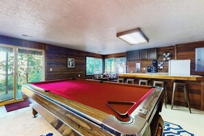 Une table de billard dans une pièce aux murs en bois, avec un coin bar.
