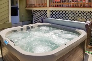Un bain à remous avec un revêtement extérieur en bois, une clôture blanche en treillis et une porte visible au fond.