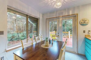 A dining area with a wooden table, chairs, and a vase. There are large windows and a view of a deck. - 3BR Dog Friendly - Hot Tub - Fireplace (Westport)