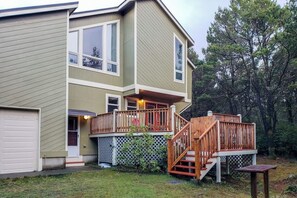 Une maison à deux étages dotée d’un porche abrité et d’un escalier en bois menant à une terrasse supérieure.