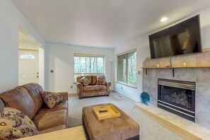 A living room with a fireplace, a large flat-screen TV, a leather sofa, and a coffee table. - 3BR Dog Friendly - Hot Tub - Fireplace (Westport)