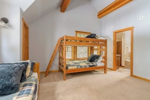 Ein Stockbett mit Holzrahmen und ein Fenster, ein Sofa mit karierter Decke sowie eine Tür zu einem Badezimmer.