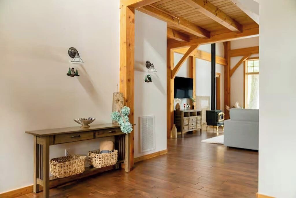 Ein raumförmiger Raum mit Holzrahmen, einem Konsolentisch, Körben, Wandleuchten und Blick in einen weiteren Raum mit einer Couch.