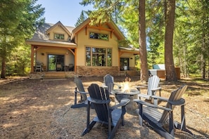 Eine Lodge mit Feuerstelle und Adirondack-Stühlen im Garten.