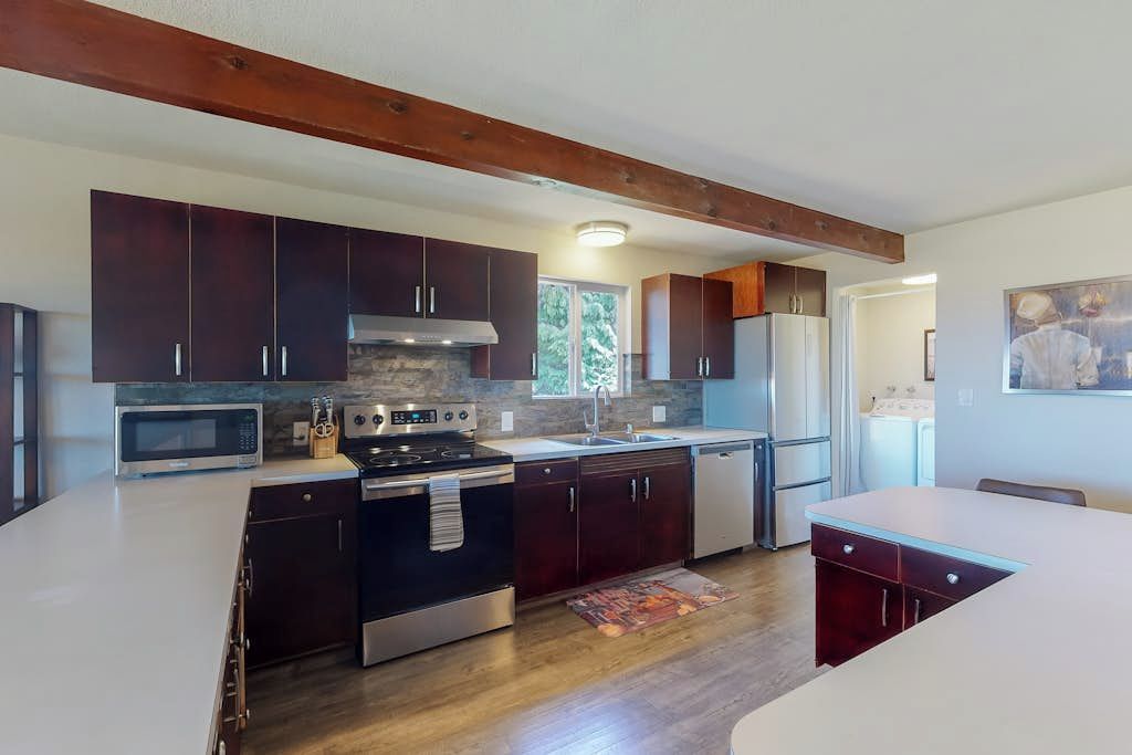 Una cucina moderna con mobili scuri, elettrodomestici in acciaio inossidabile e un trave in legno al soffitto.