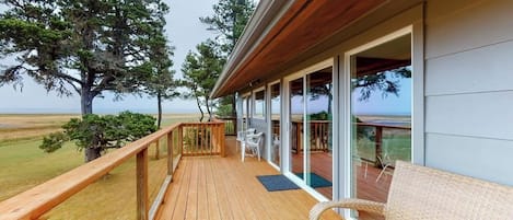 A wooden deck with a glass railing overlooking a grassy area and trees.